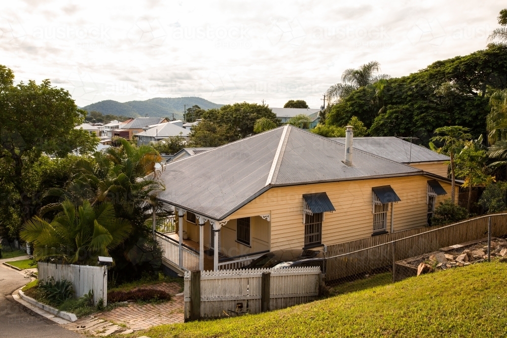 yellow painted Queenslander house with a metal roof on the side of a hill - Australian Stock Image