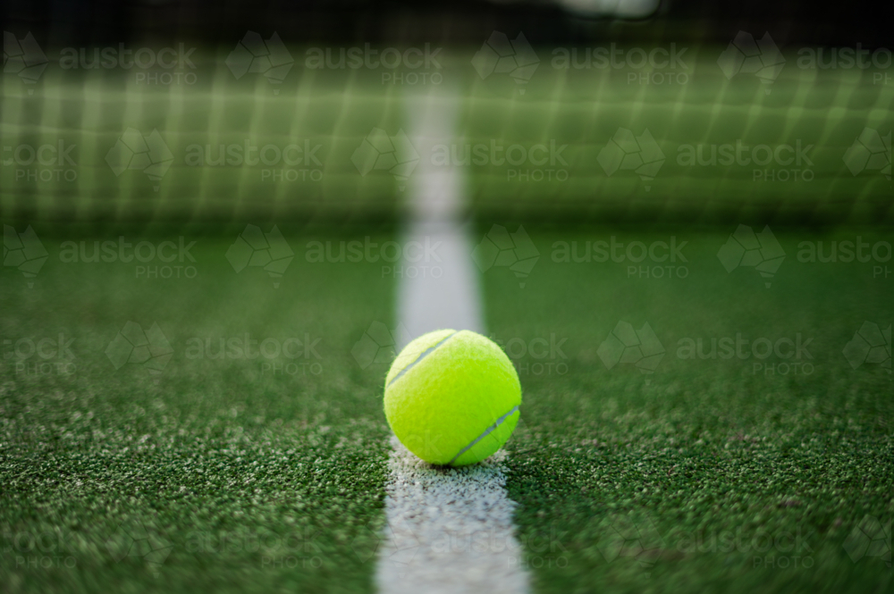 Yellow tennis ball rests on white line of artificial grass court before tennis match - Australian Stock Image