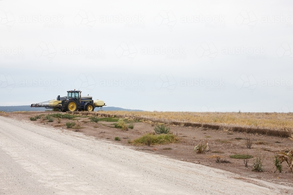 yellow tractor in an empty field and road - Australian Stock Image