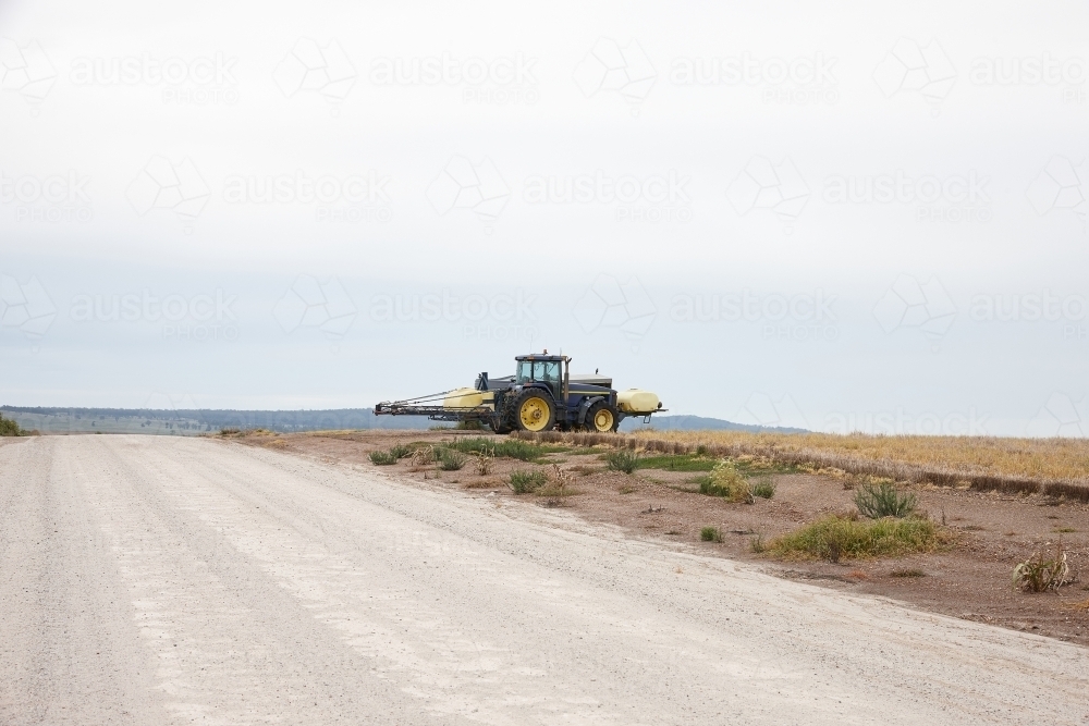 yellow tractor in an empty field and road - Australian Stock Image