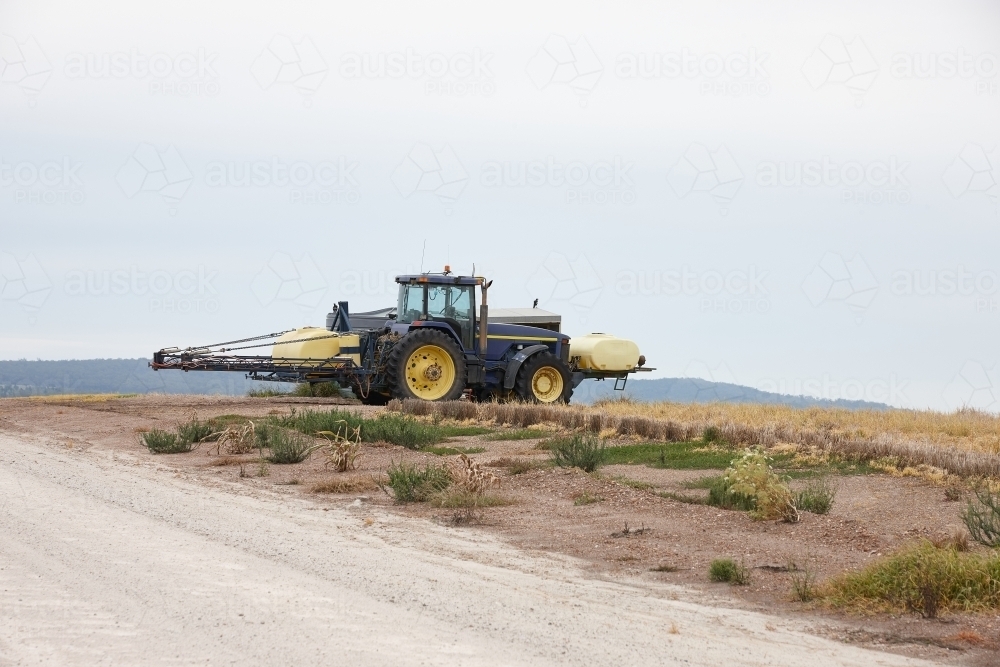 yellow tractor in an empty field and road - Australian Stock Image