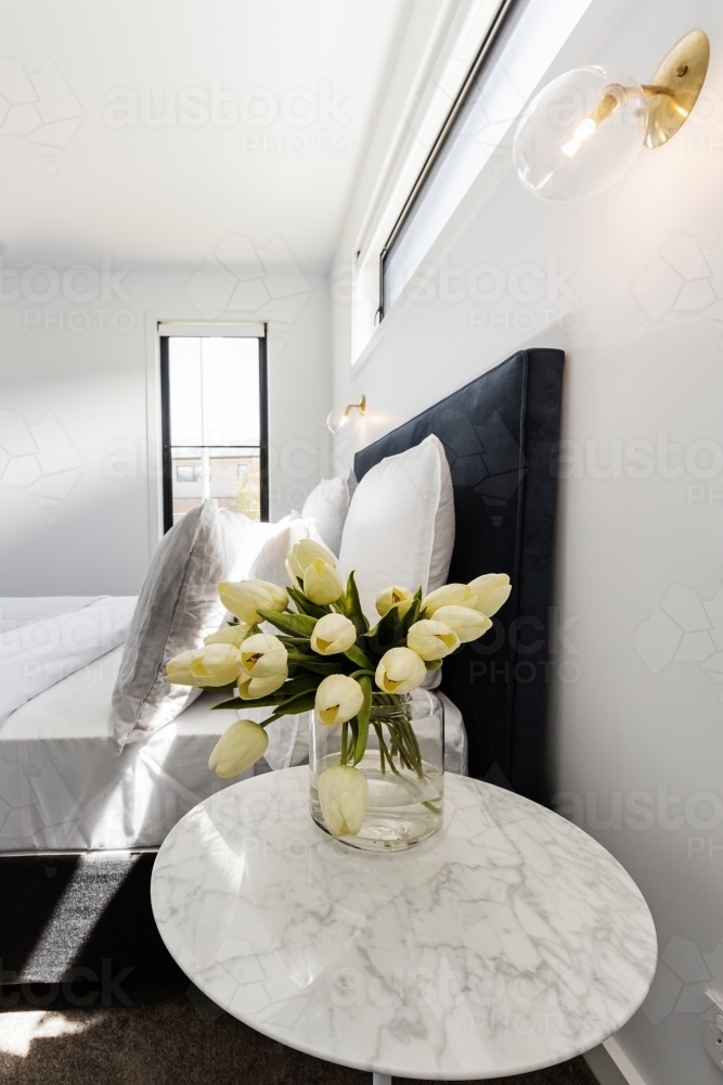 Yellow tulips on a bedside table with gold wall light above - Australian Stock Image