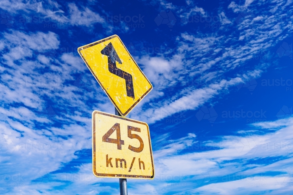Yellow winding road warning sign with blue sky background - Australian Stock Image
