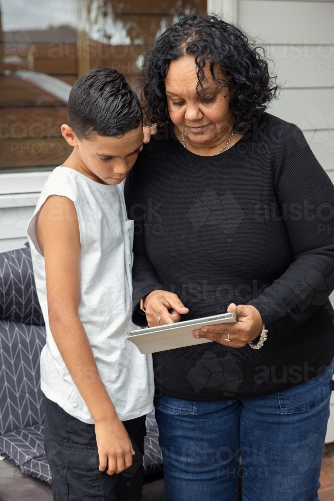 Young Aboriginal boy and Aboriginal woman looking at a device outside - Australian Stock Image