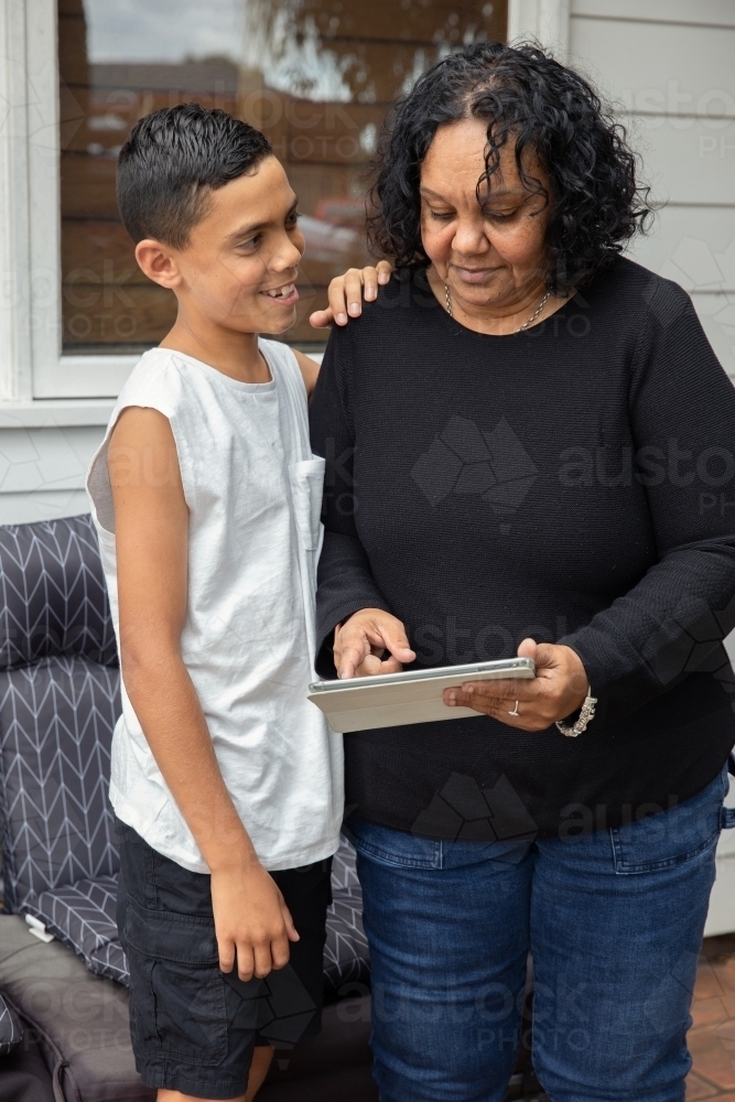 Young Aboriginal boy and Aboriginal woman looking at a device outside - Australian Stock Image