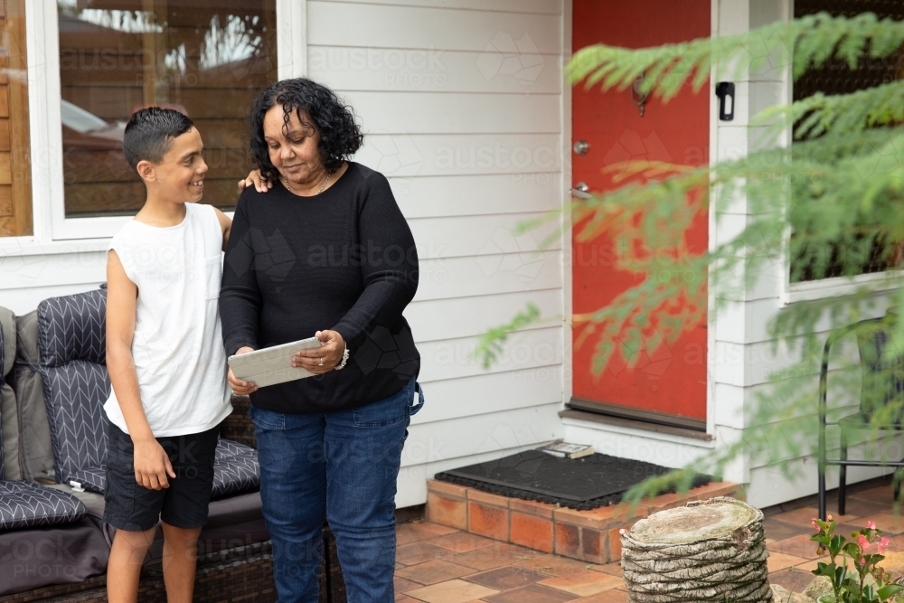 Young Aboriginal boy and Aboriginal woman looking at a device outside - Australian Stock Image