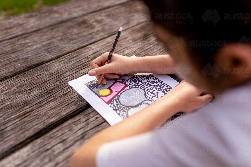 Young Aboriginal boy colouring in an Aboriginal flag with pencils - Australian Stock Image