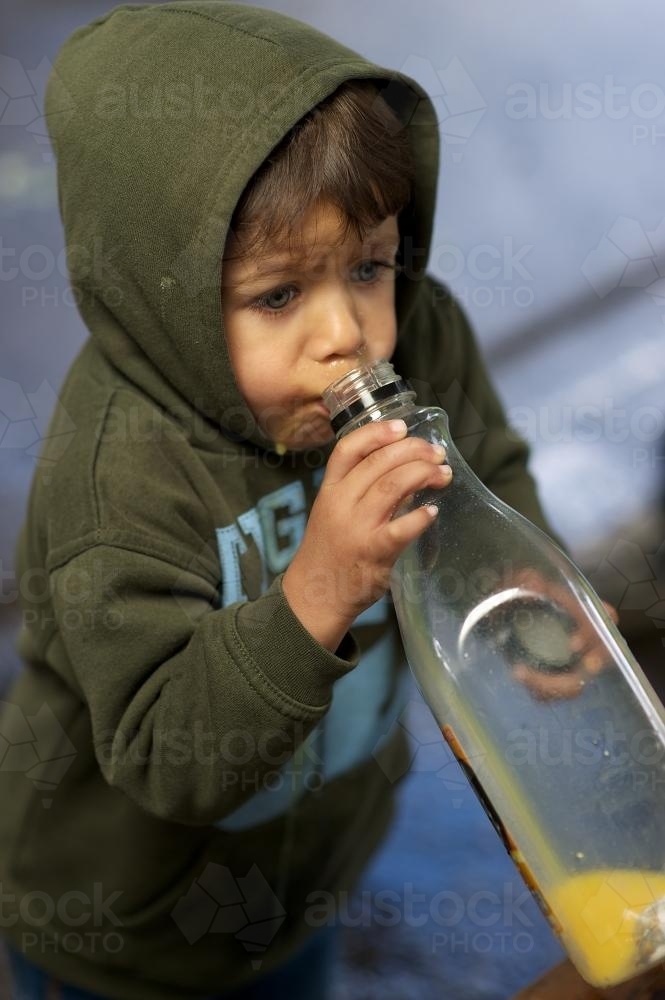 Young Aboriginal Boy in Green Top Drinking From Large Juice Bottle - Australian Stock Image
