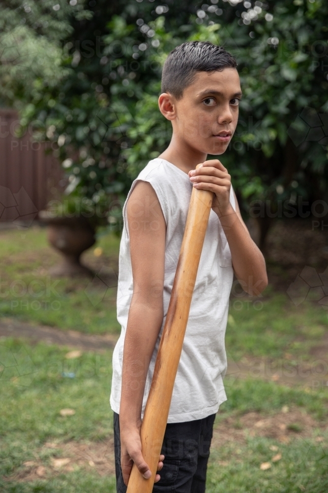 Young Aboriginal boy playing a didgeridoo in the backyard - Australian Stock Image
