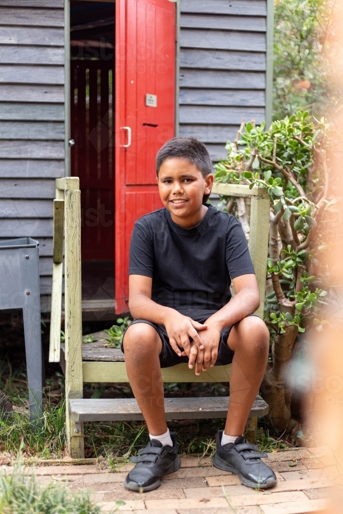 Young Aboriginal boy sitting on stairs in the backyard - Australian Stock Image