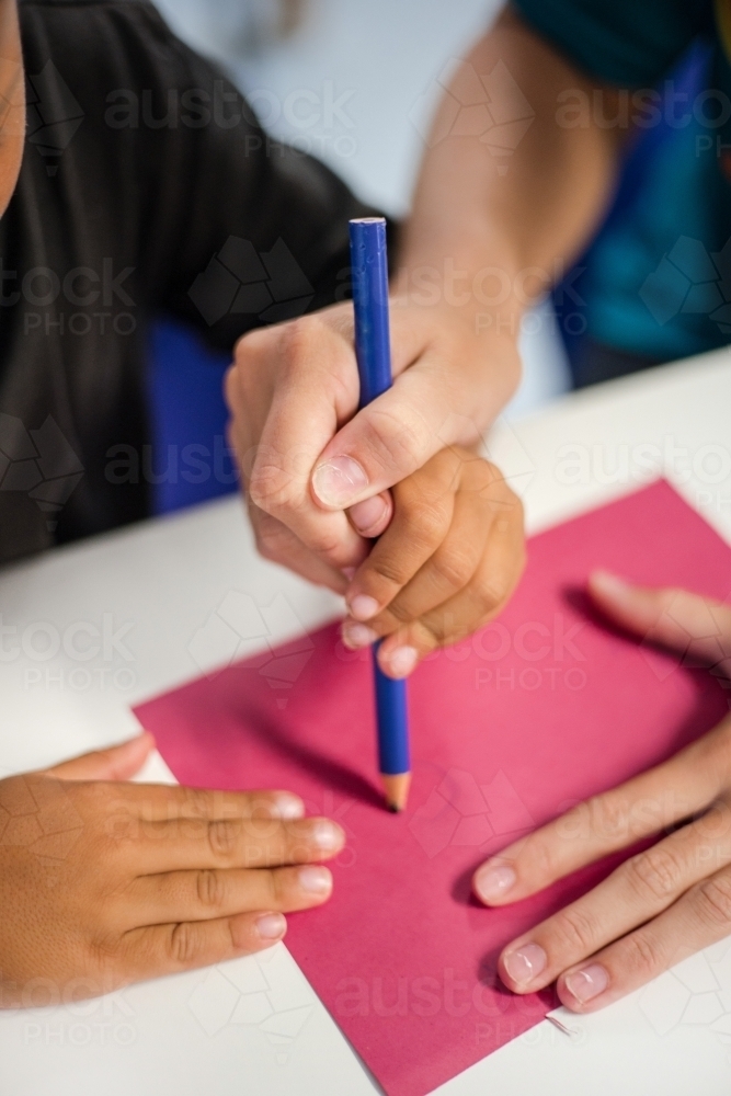 Young Aboriginal boy writing with teacher - Australian Stock Image