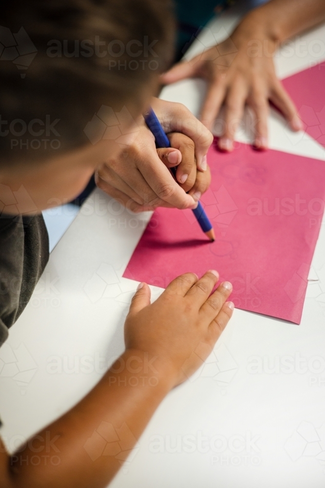 Young Aboriginal boy writing with teacher - Australian Stock Image