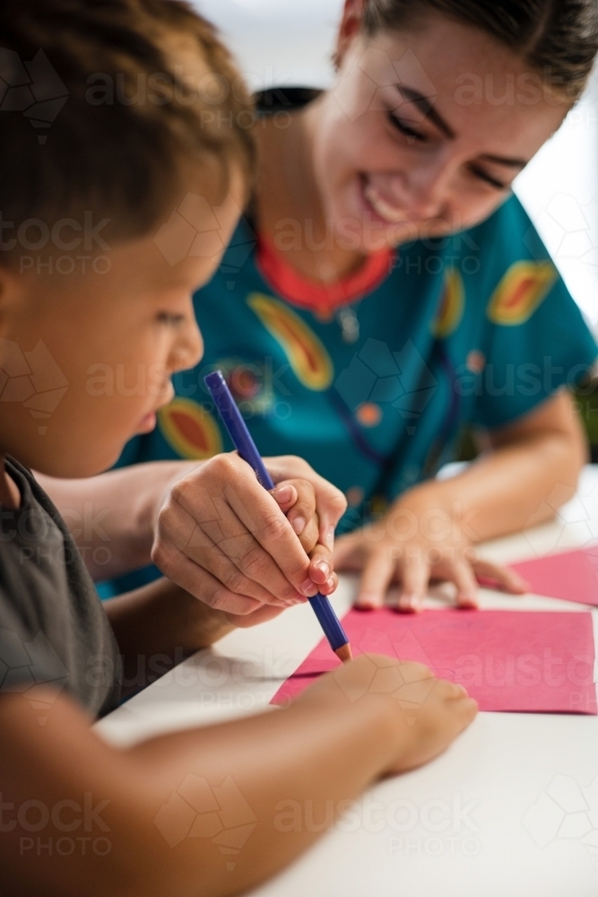 Young Aboriginal boy writing with teacher - Australian Stock Image
