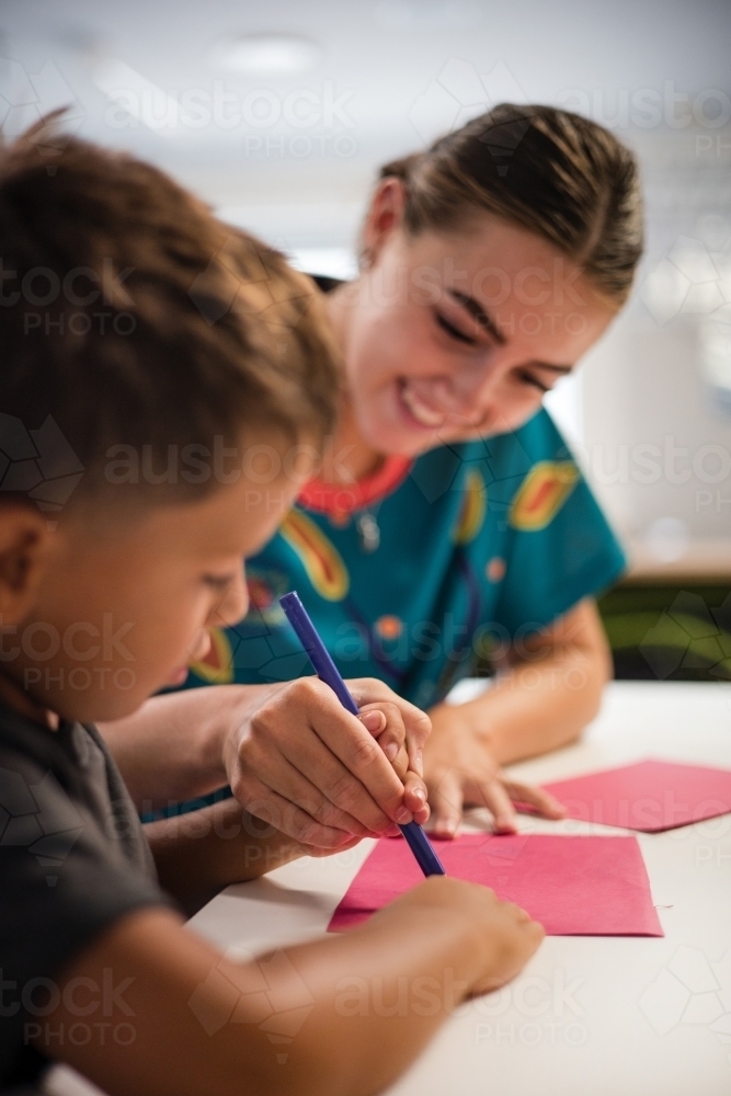 Young Aboriginal boy writing with teacher - Australian Stock Image