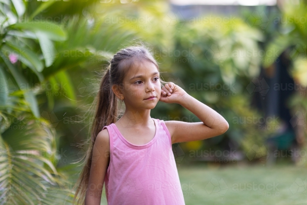young aboriginal child with long hair in ponytail in garden - Australian Stock Image