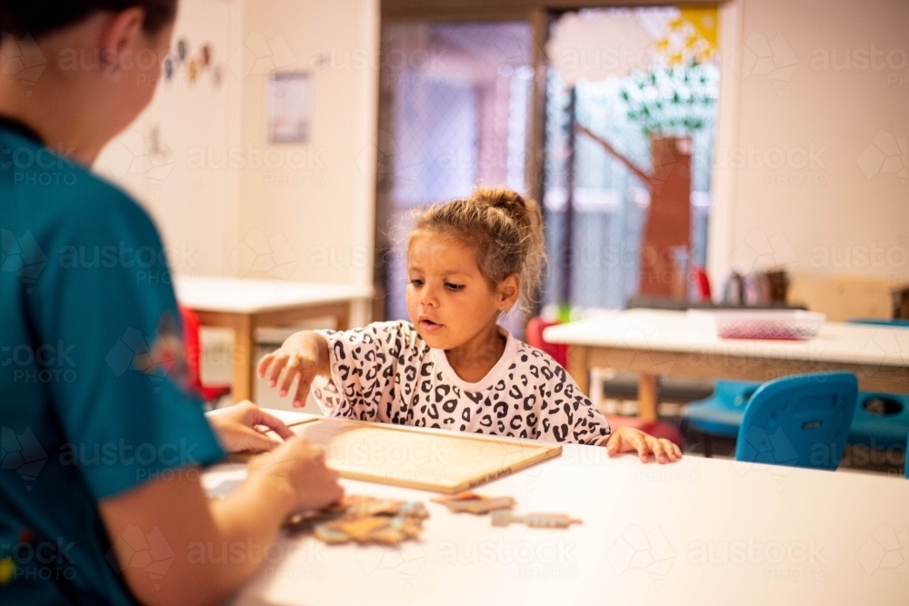 Young Aboriginal girl at preschool doing a puzzle with a teacher - Australian Stock Image