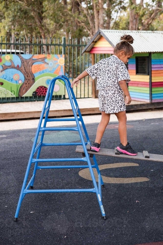 Young Aboriginal girl climbing over a ladder at preschool - Australian Stock Image