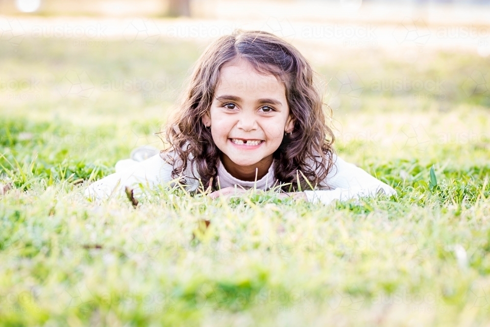 Young aboriginal girl laying in grass smiling - Australian Stock Image