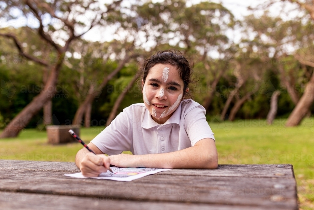 Young Aboriginal girl sitting at table drawing and smiling at the camera - Australian Stock Image