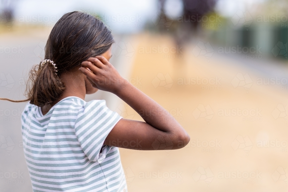 young aboriginal girl standing side-on incognito with hand to head - Australian Stock Image