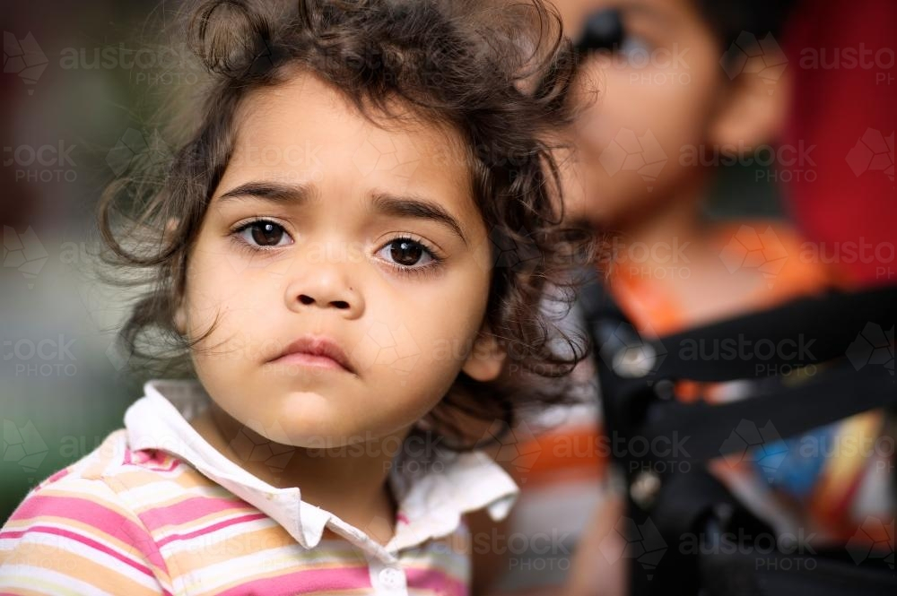 Young aboriginal girl with wavy hair wearing pink stripe shirt. - Australian Stock Image
