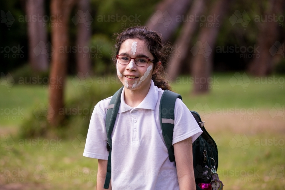 Young Aboriginal girl with white face paint wearing glasses and a backpack - Australian Stock Image