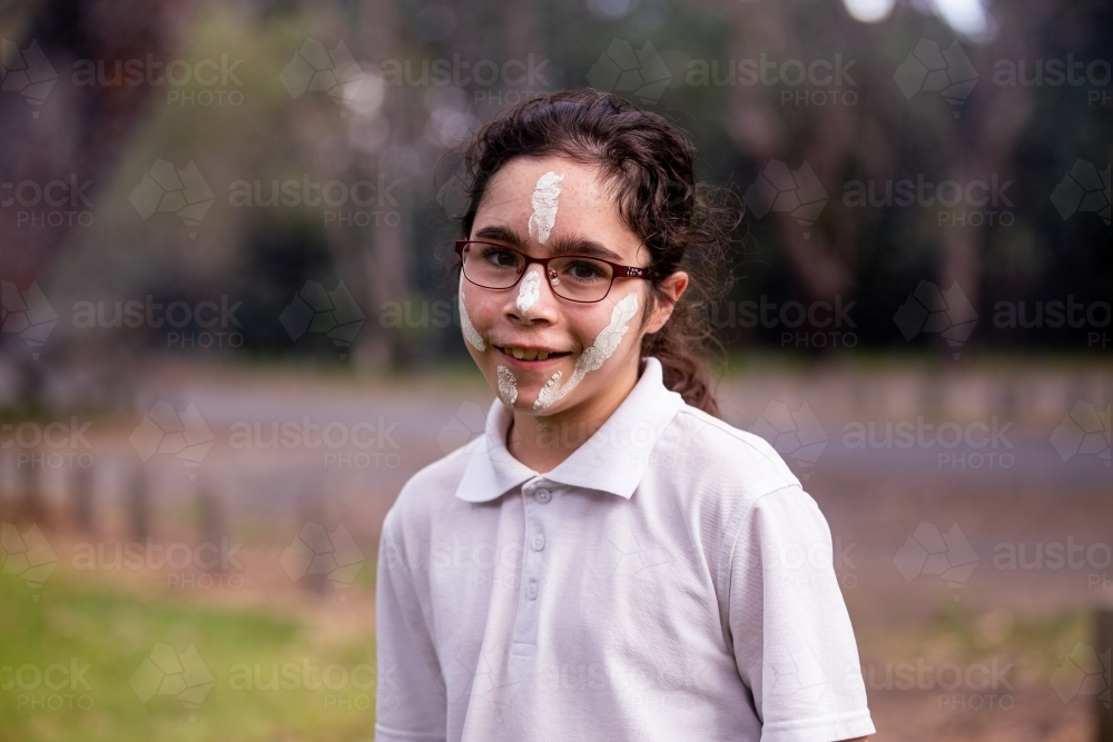 Young Aboriginal girl with white face paint wearing glasses and a backpack - Australian Stock Image