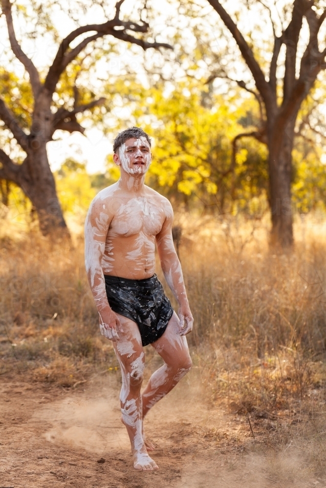 Young Aboriginal man wearing ochre body paint and a lap lap standing in Australian bushland - Australian Stock Image