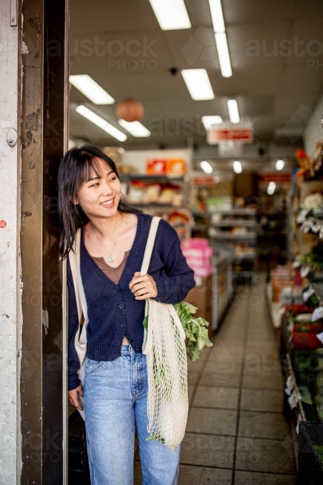 Young adult asian woman standing at the door of a small local grocery store - Australian Stock Image