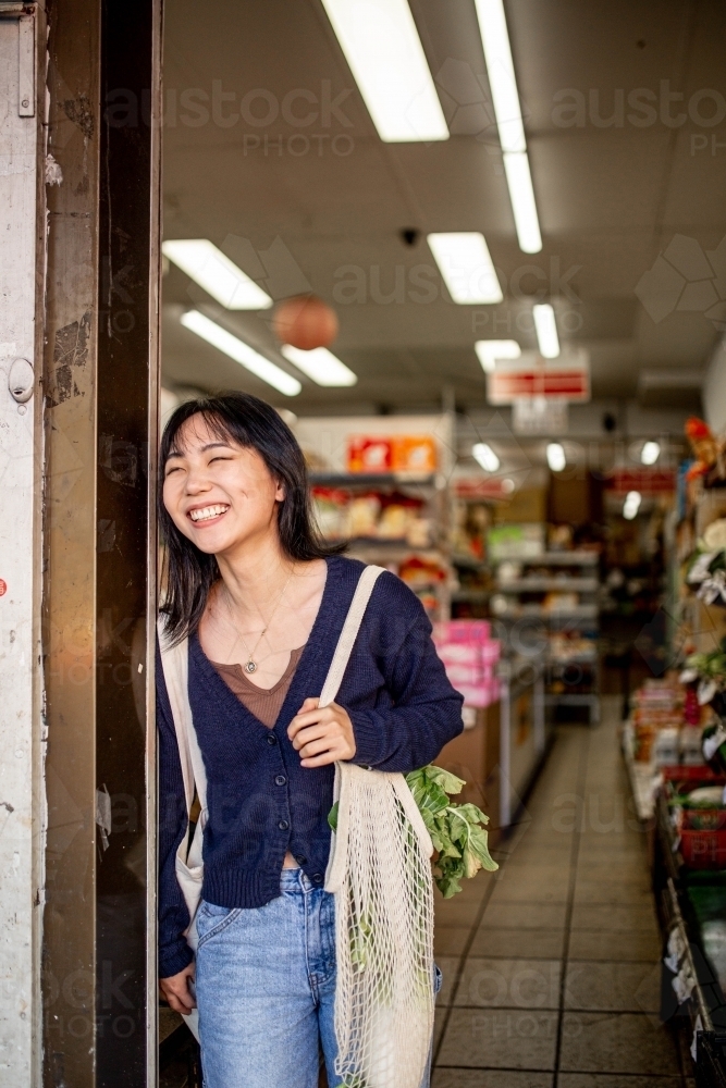 Young adult asian woman standing at the door of a small local grocery store - Australian Stock Image