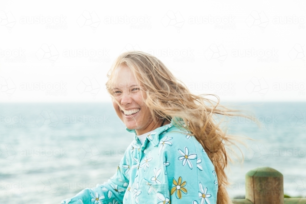 Young adult looking out over the ocean laughing with wind blowing her hair - Australian Stock Image