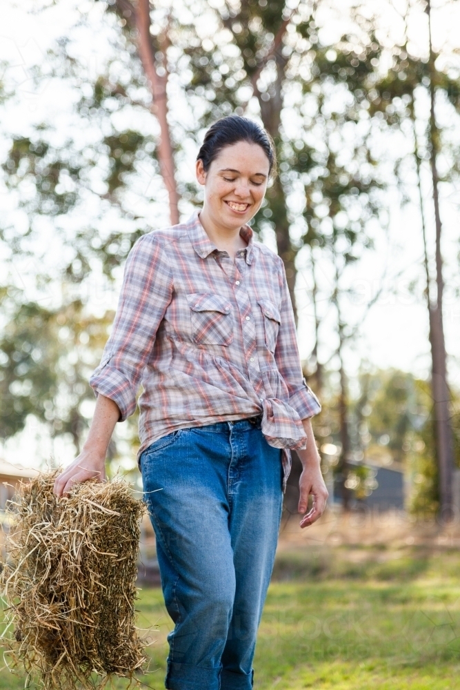 Young adult person carrying hay biscuit to feed animals - Australian Stock Image