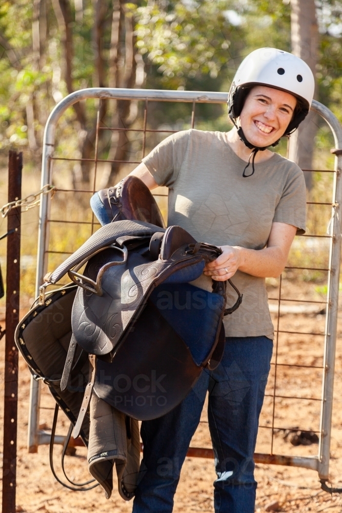 Young adult person in her twenties carrying horses saddle - Australian Stock Image