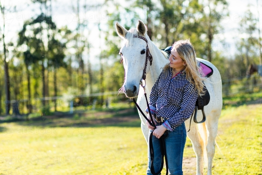 Young adult talking to her horse in paddock - Australian Stock Image