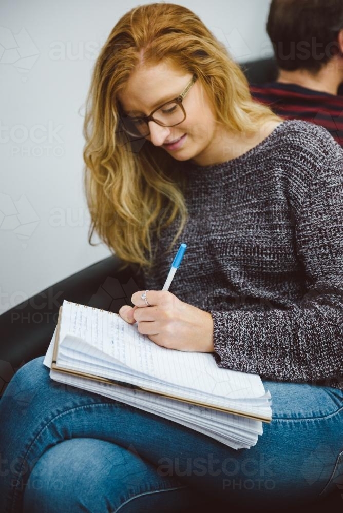 Young adult with glasses writing notes at university - Australian Stock Image