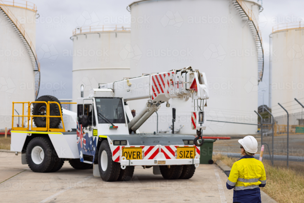 Young adult woman in reflective clothing standing in front of a crane truck - Australian Stock Image