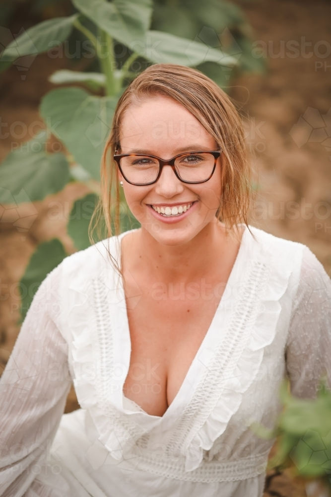 Young adult woman sitting in sunflower field - Australian Stock Image