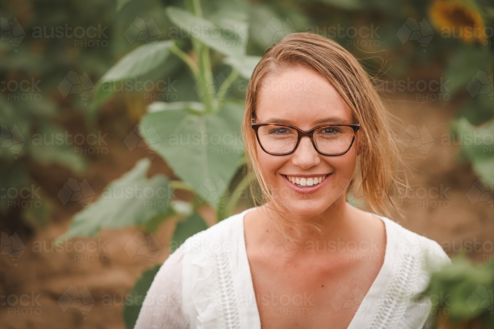 Young adult woman sitting in sunflower field - Australian Stock Image