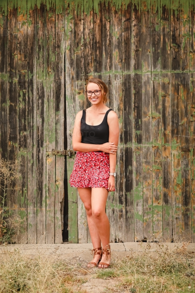 Young adult woman standing in front of rustic barn door with chipped paint - Australian Stock Image