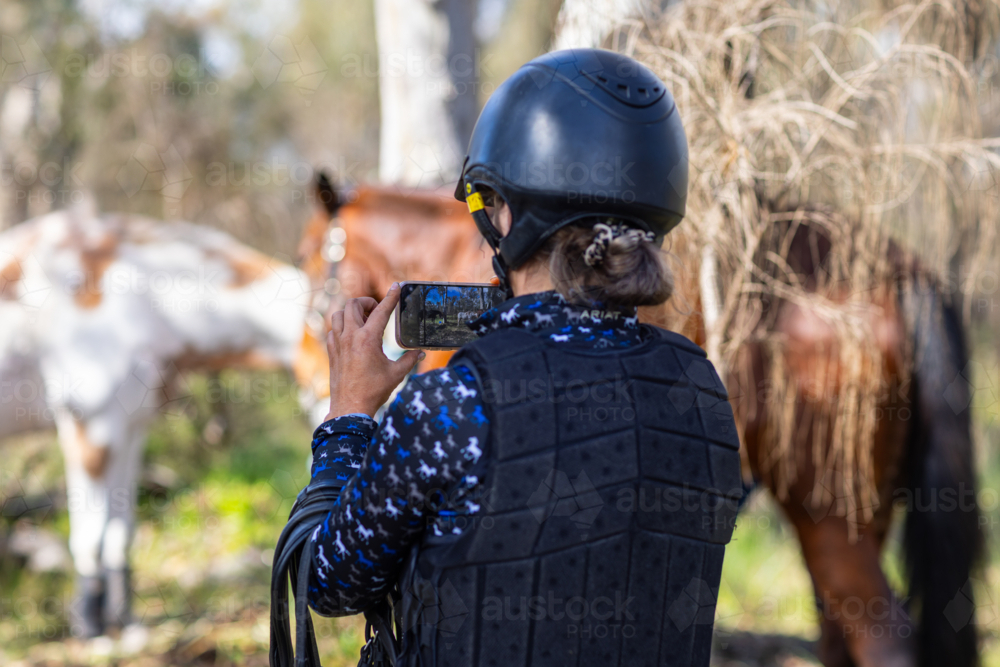 Young adult woman taking photos of horses outdoors. - Australian Stock Image
