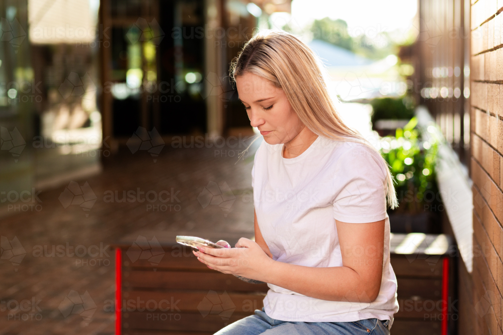 young adult woman using mobile phone device scrolling on social media sitting in urban alleyway - Australian Stock Image