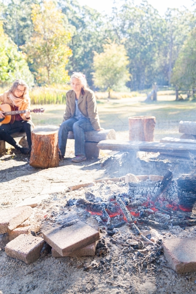 Young adults sitting around campfire in the morning - Australian Stock Image