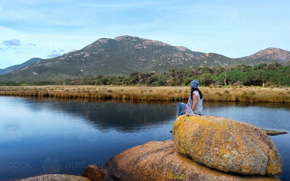 Young adventurer sitting on a rock beside a river - Australian Stock Image