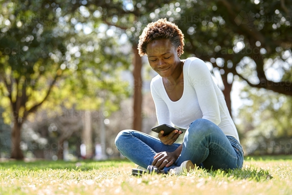 Young African woman enjoying time in sunshine on mobile phone - Australian Stock Image