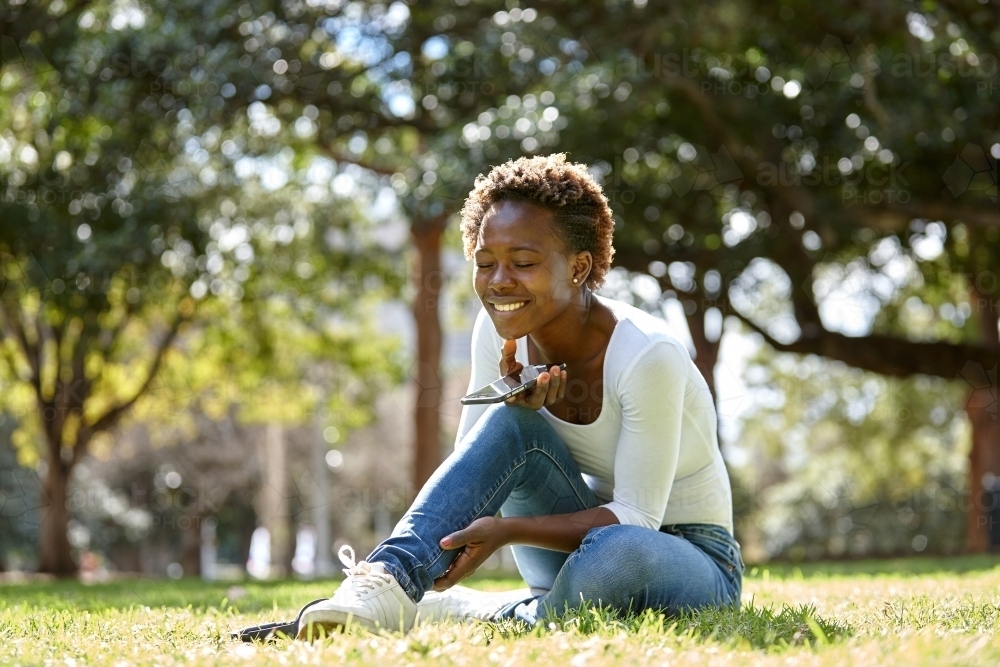 Young African woman enjoying time in sunshine with mobile phone - Australian Stock Image
