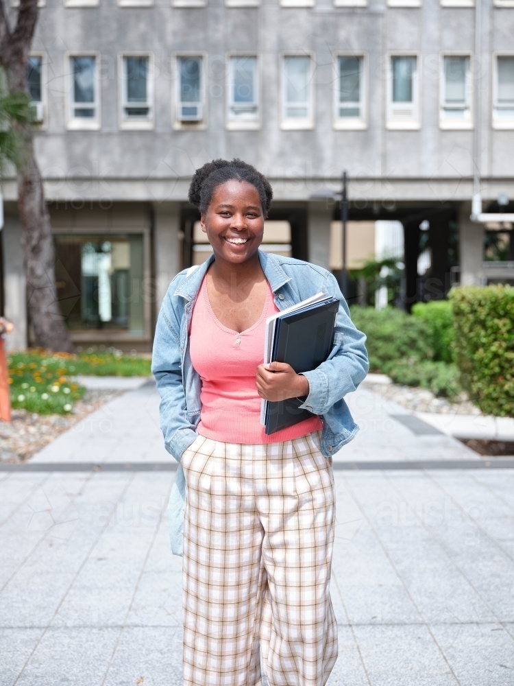 Young African woman holding books in university courtyard - Australian Stock Image