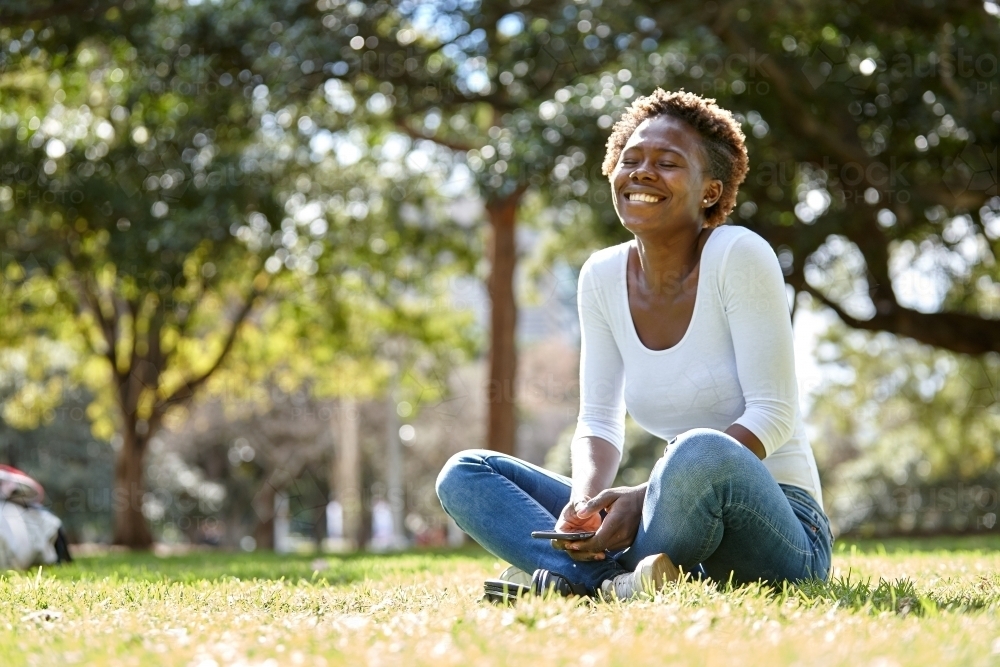 Young African woman laughing at park in sunshine - Australian Stock Image