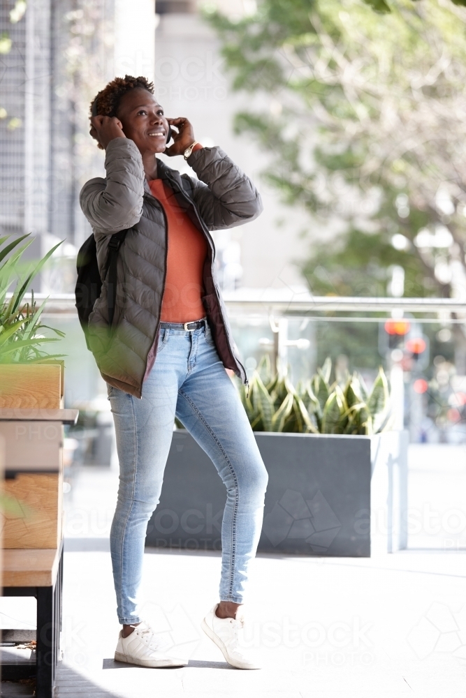 Young African woman listening to music wearing wireless headphones in city - Australian Stock Image