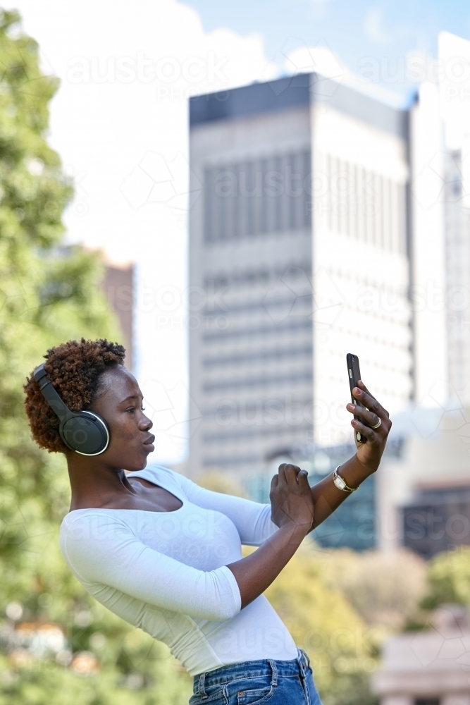 Young African woman listening to music wearing wireless headphones in city - Australian Stock Image