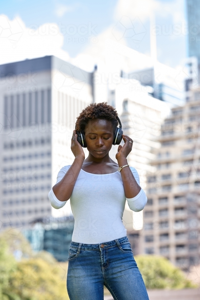 Young African woman listening to music wearing wireless headphones in city - Australian Stock Image